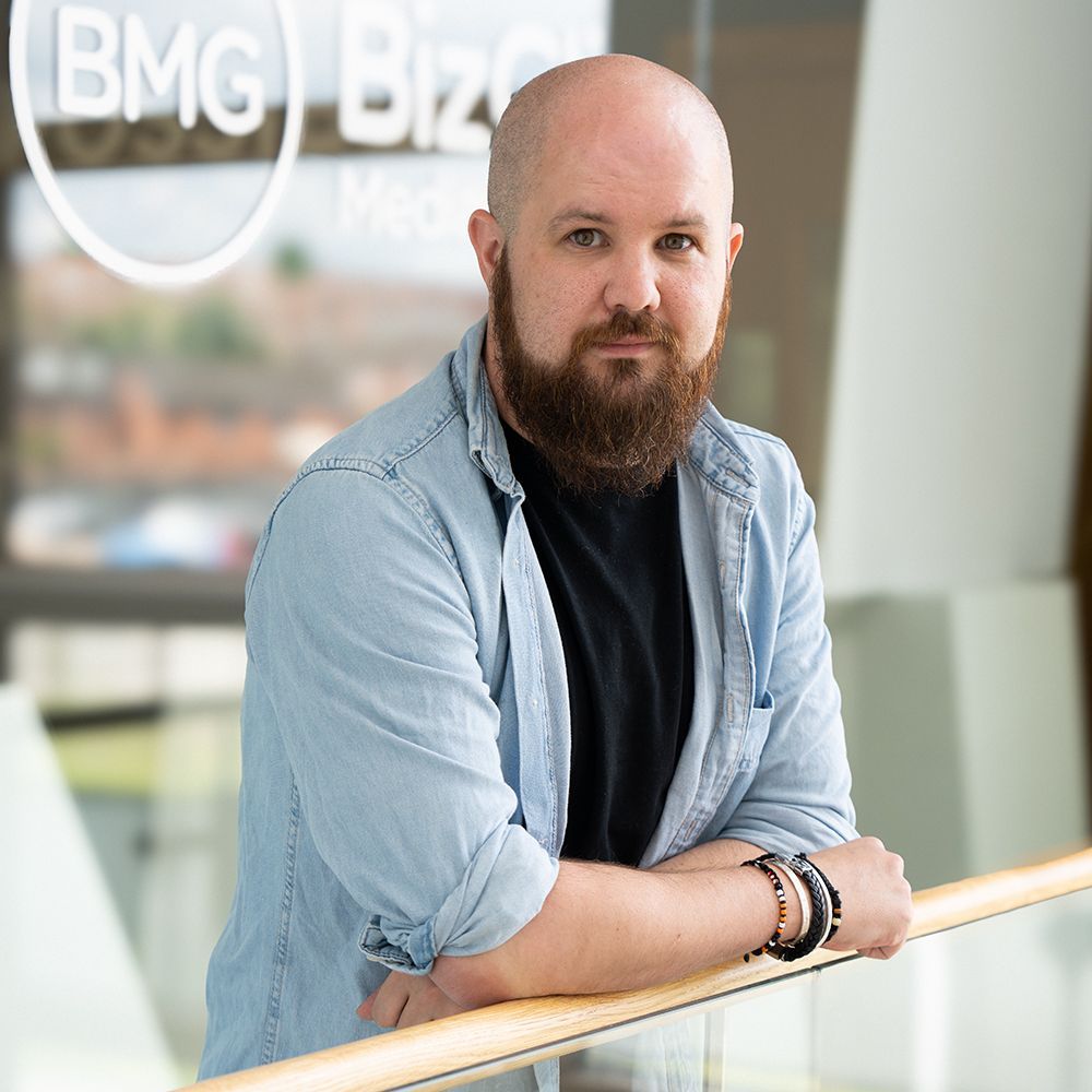 A bald man with a beard is leaning on a railing.