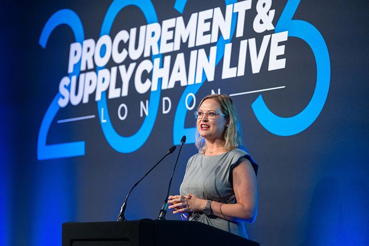 A woman is standing at a podium giving a speech at a procurement and supply chain live event.