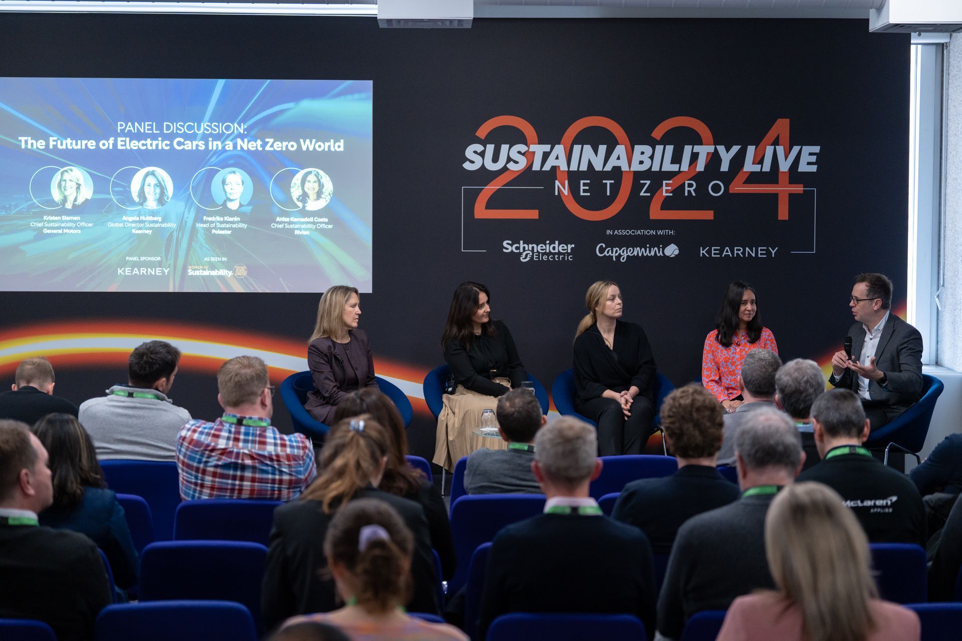 A group of people are sitting in chairs in front of a large screen at sustainability live 2024.
