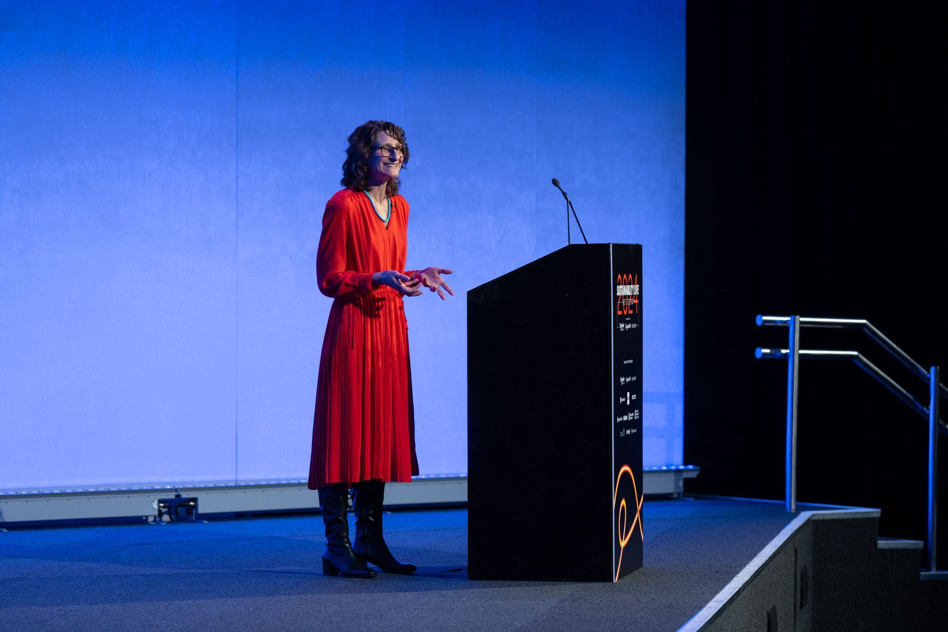 Courtney Holm, VP of Sustainable Futures at Capgemini Invent in a red dress is standing on stage at Sustainability LIVE Net Zero