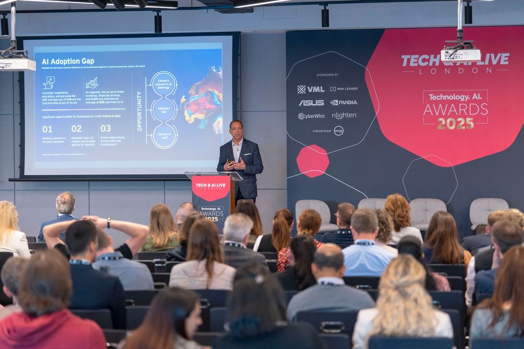 A man is standing at a podium giving a presentation at tech & ai live london.