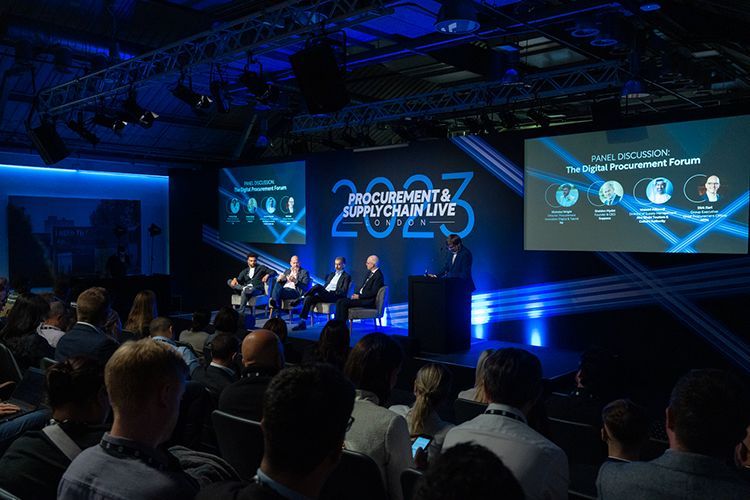 A group of people are sitting in front of a stage at a conference.