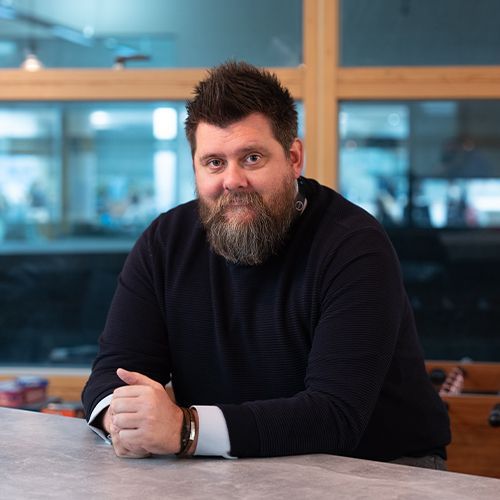 A man with a beard is sitting at a table with his hands folded.