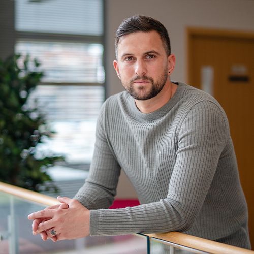 A man with a beard is leaning on a railing and looking at the camera.