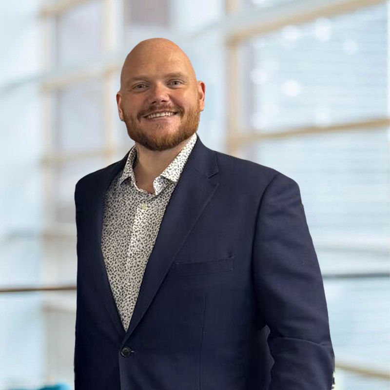 A bald man with a beard and tattoos is leaning on a railing.