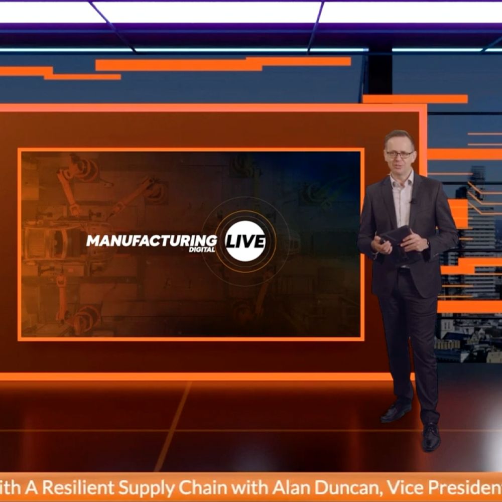 A man stands in front of a screen that says manufacturing live