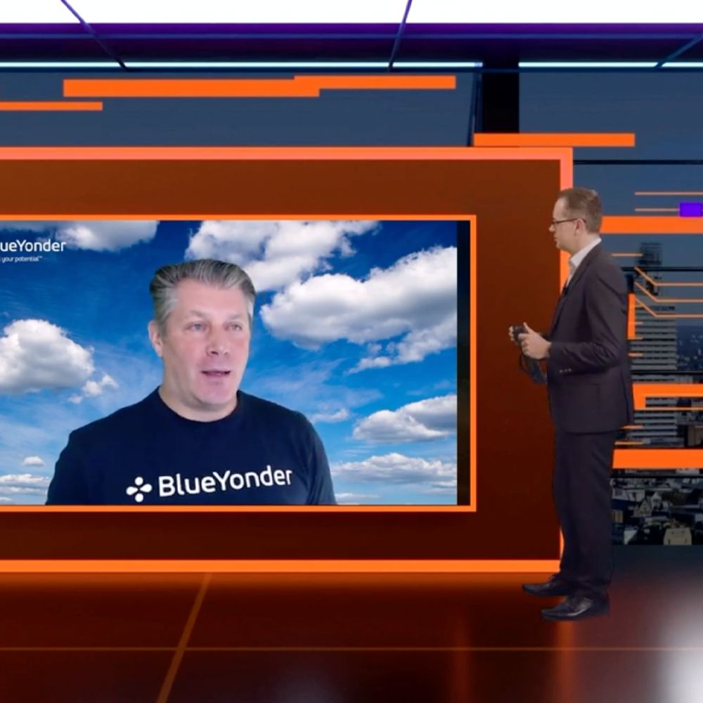 A man wearing a blue yonder shirt stands in front of a large screen