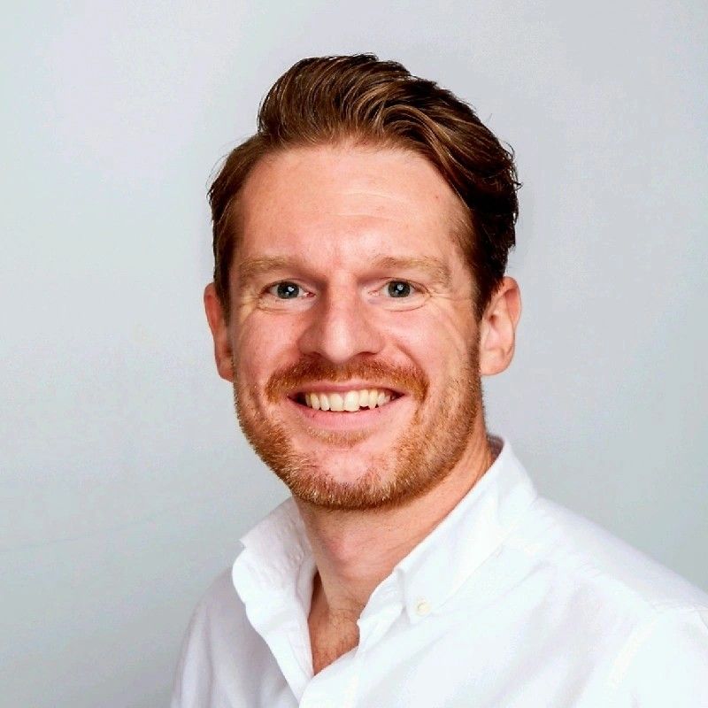 A man with a beard is sitting at a table with his hands folded.