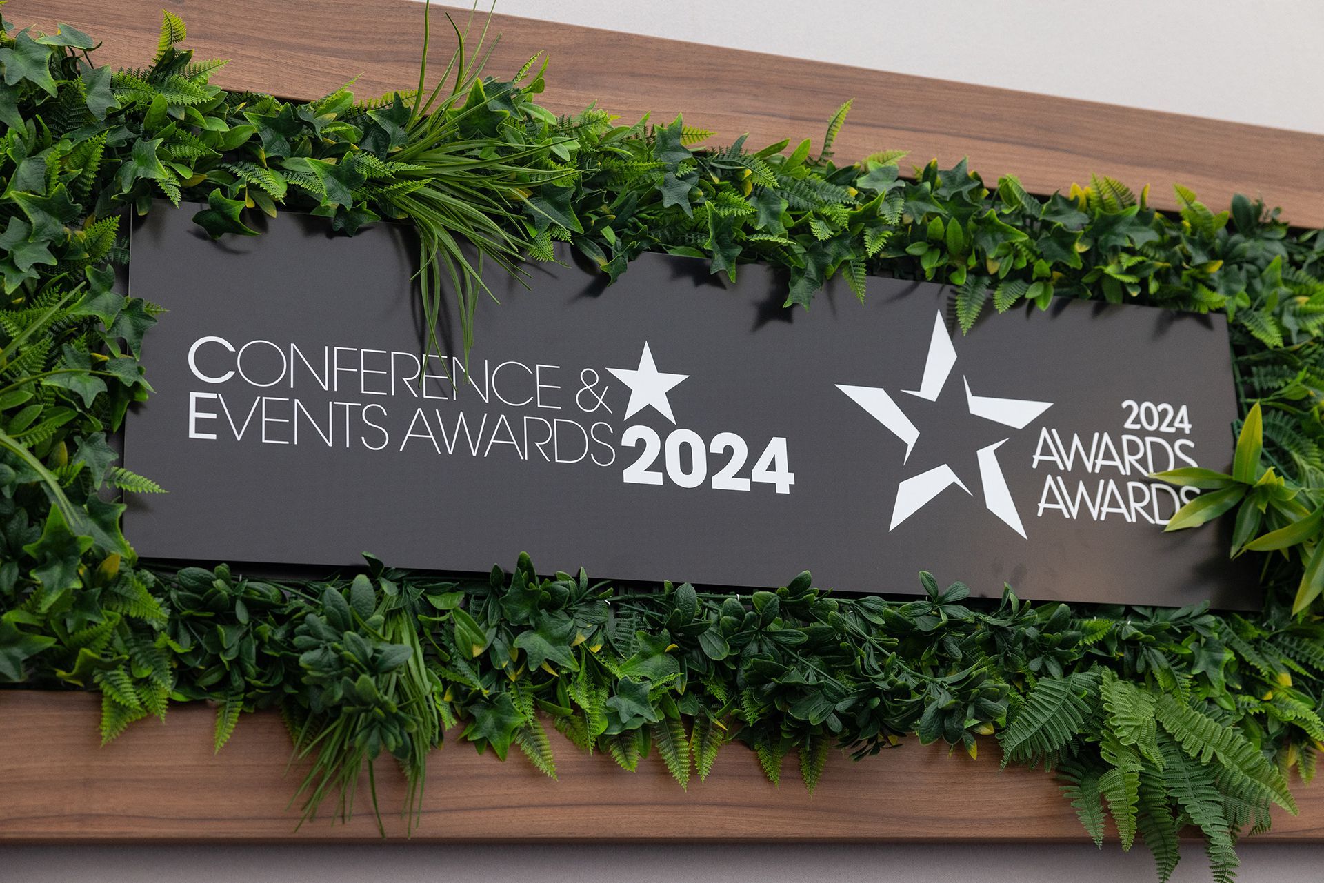 A sign for the conference and events awards 2024 is surrounded by greenery.