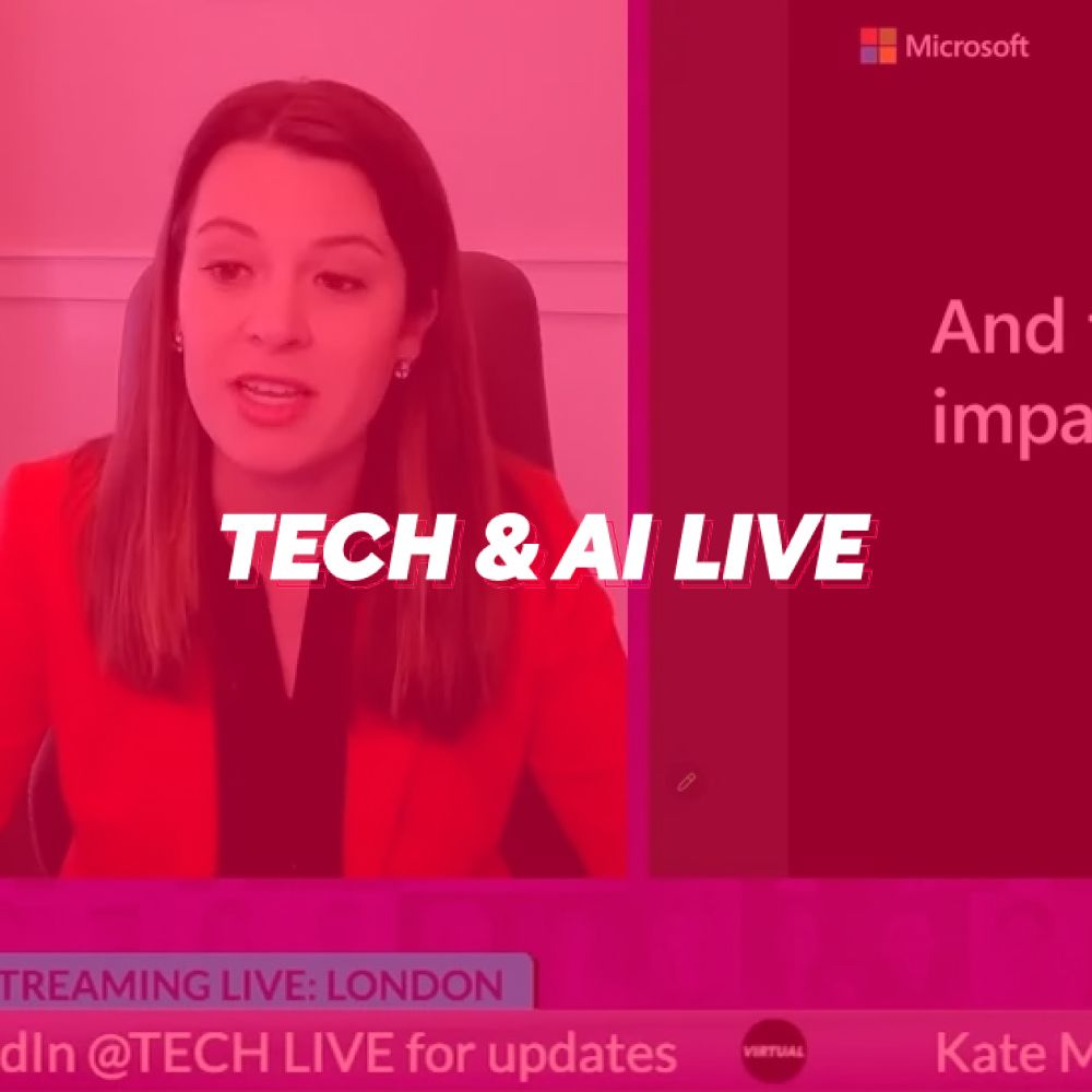 A woman in a red jacket is sitting in front of a screen that says tech & ai live