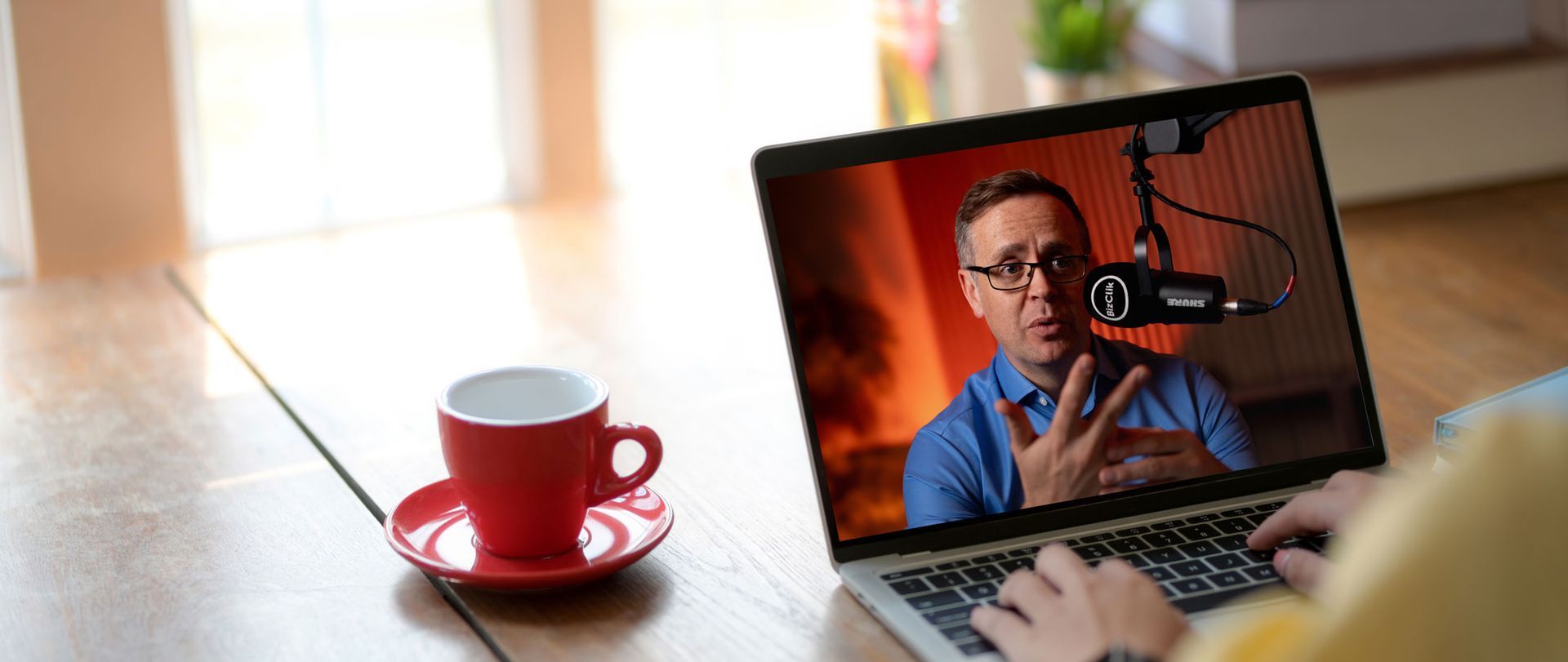 Man speaking on webinar with microphone, viewed on laptop with coffee cup on desk