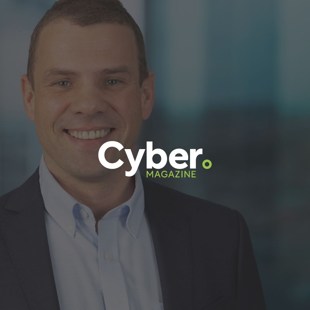 A man is smiling in front of a cyber magazine logo