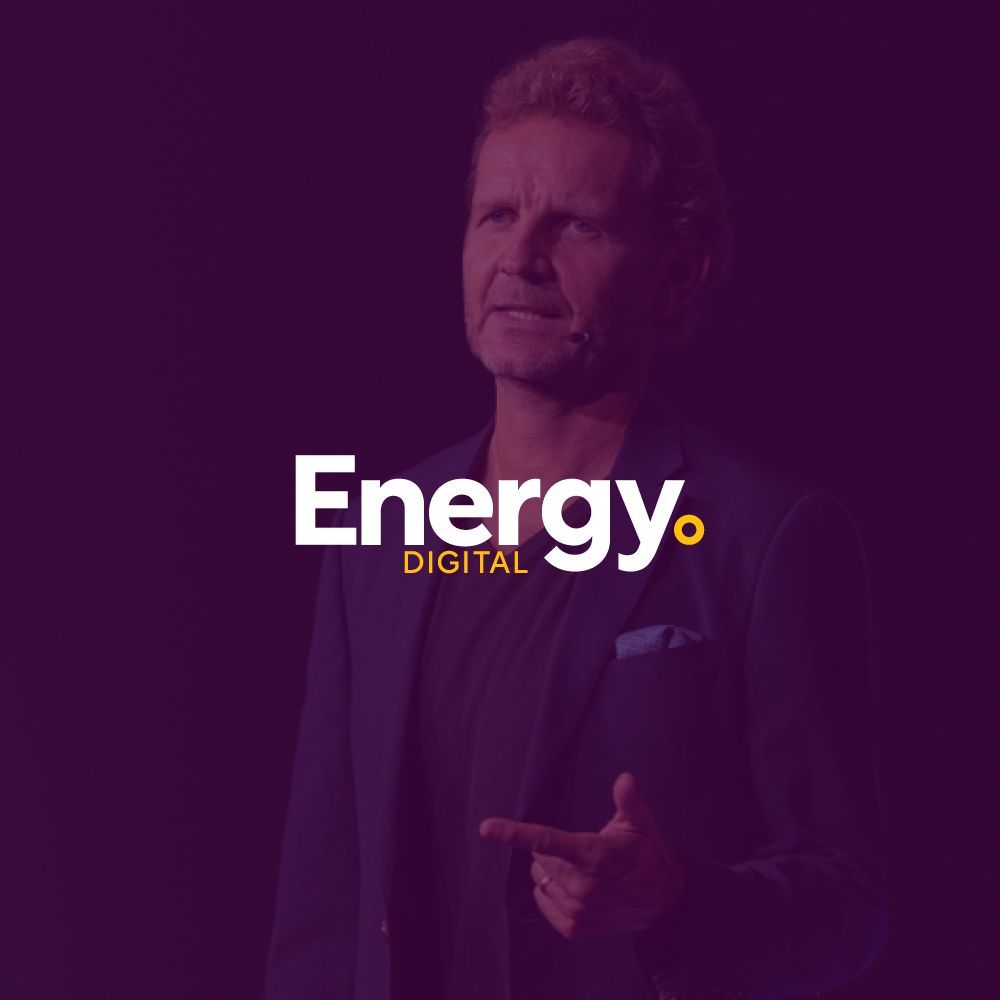 A man in a suit is standing in front of a purple background.