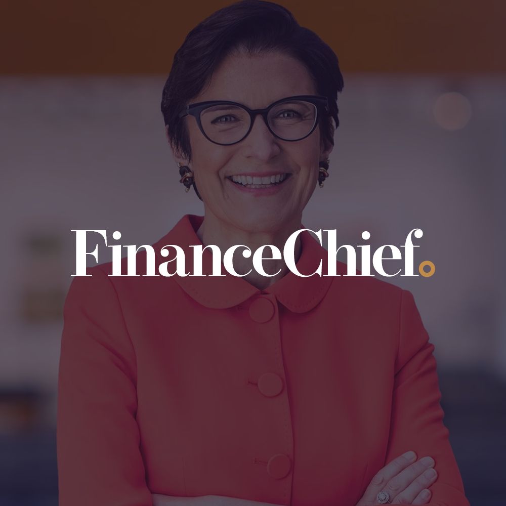 A woman wearing glasses and a red coat is smiling for the finance chief