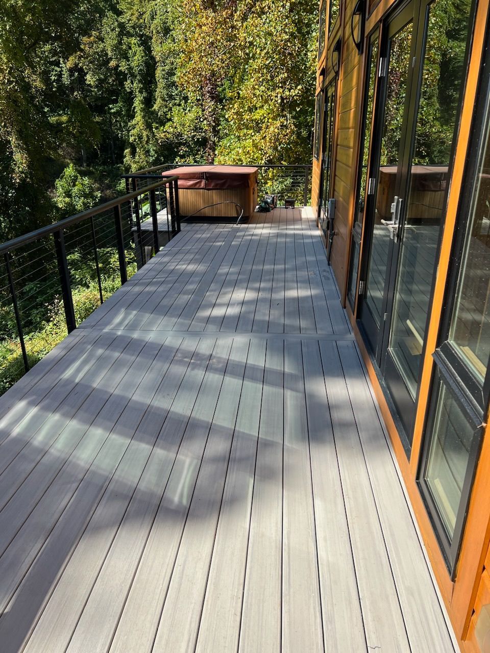 A large deck with a hot tub on it is surrounded by trees.