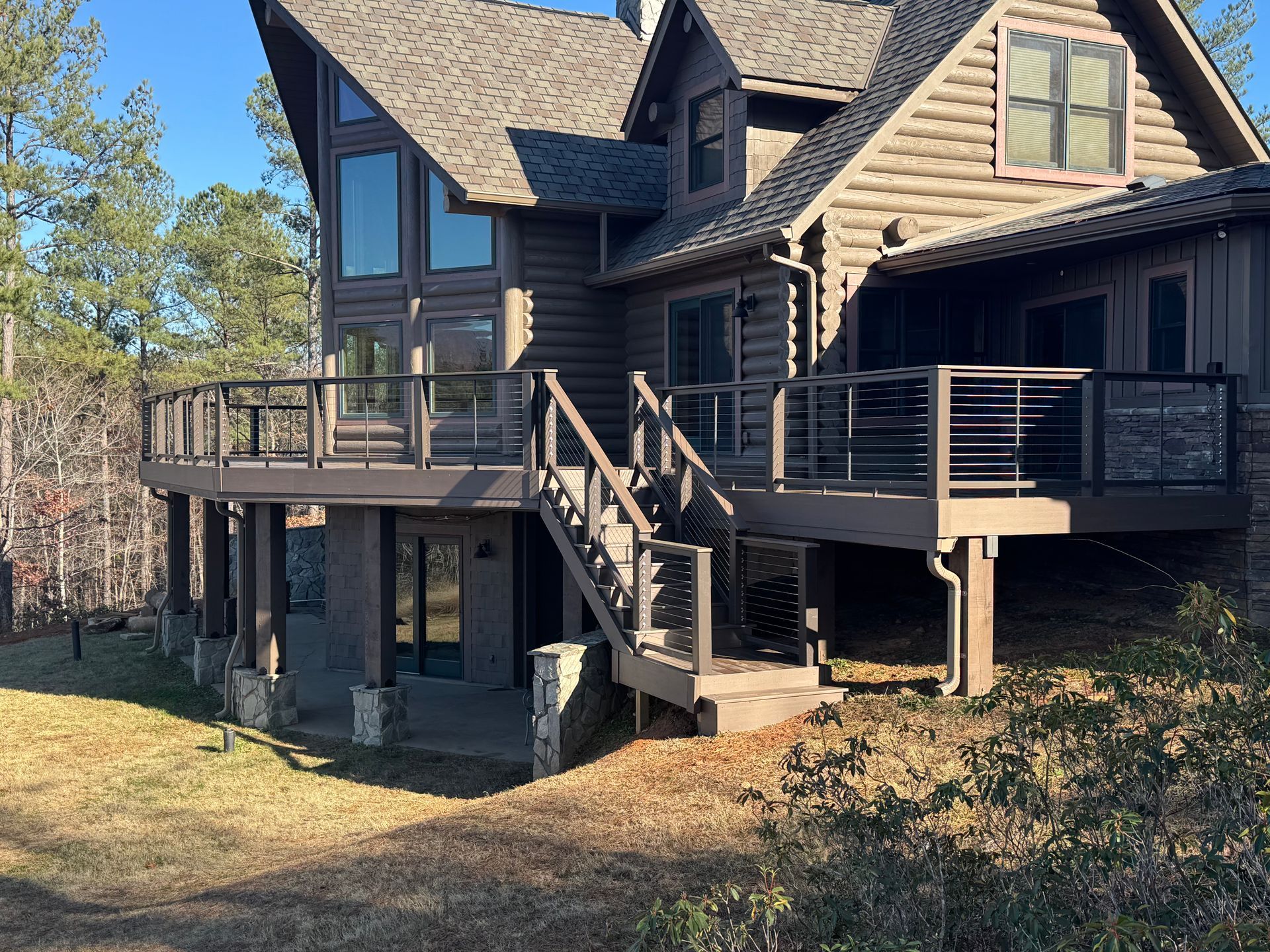 A large log cabin with a large deck and stairs leading up to it.