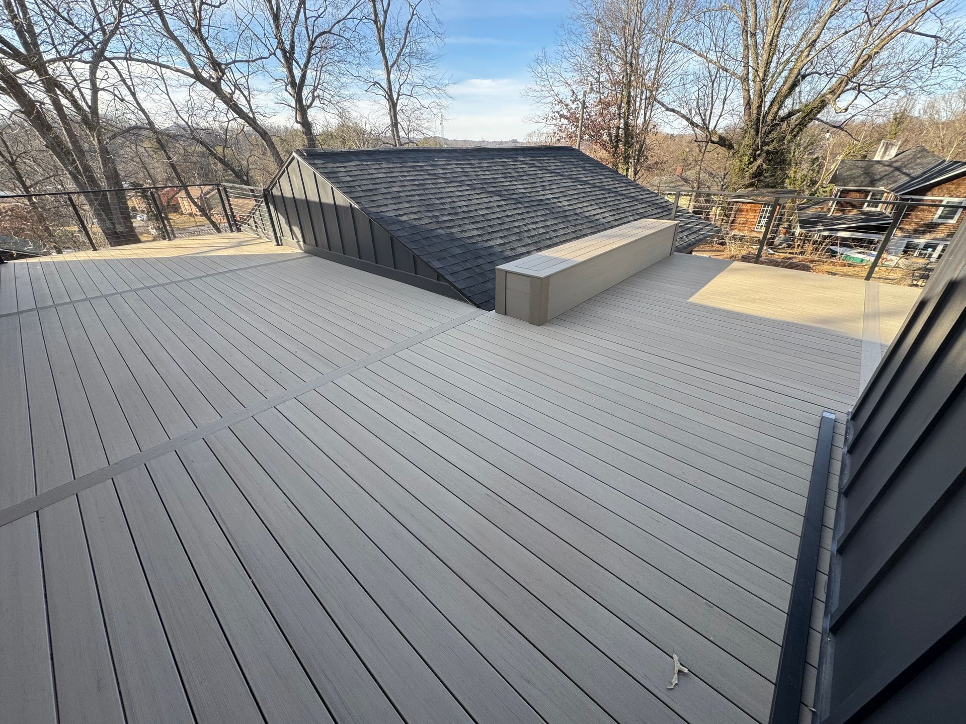 A large gray deck with a black roof and trees in the background.