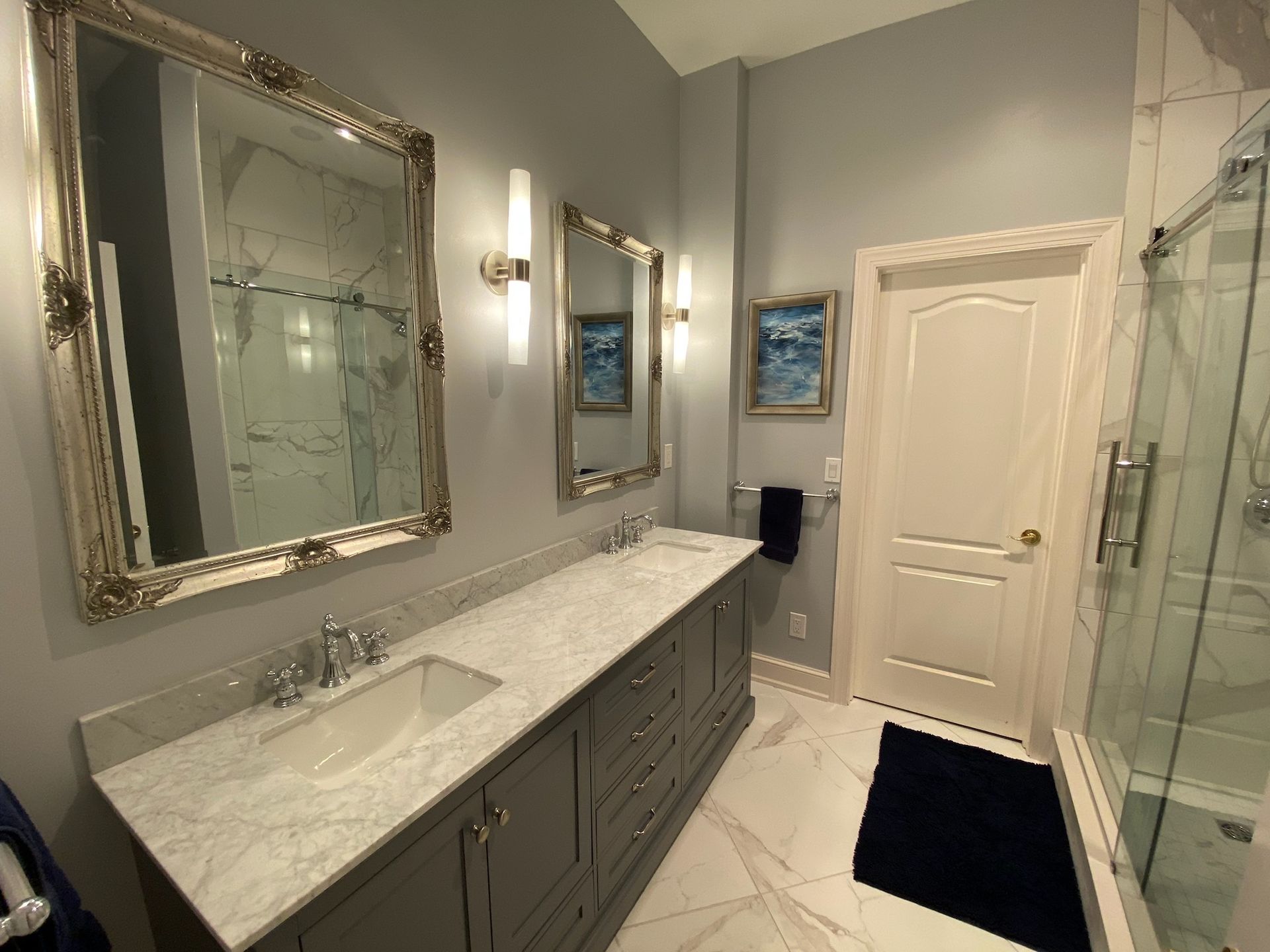 A bathroom with two sinks , two mirrors and a walk in shower.