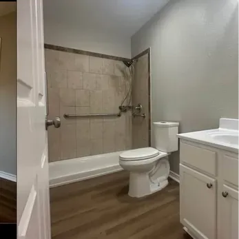 Bathroom with shower, toilet, and vanity. Beige tile shower with grab bar, white toilet, and white vanity.