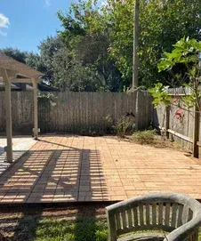 Backyard patio with wooden tiles, a gazebo, and wooden fence. Sunlight casts shadows on the tiles.