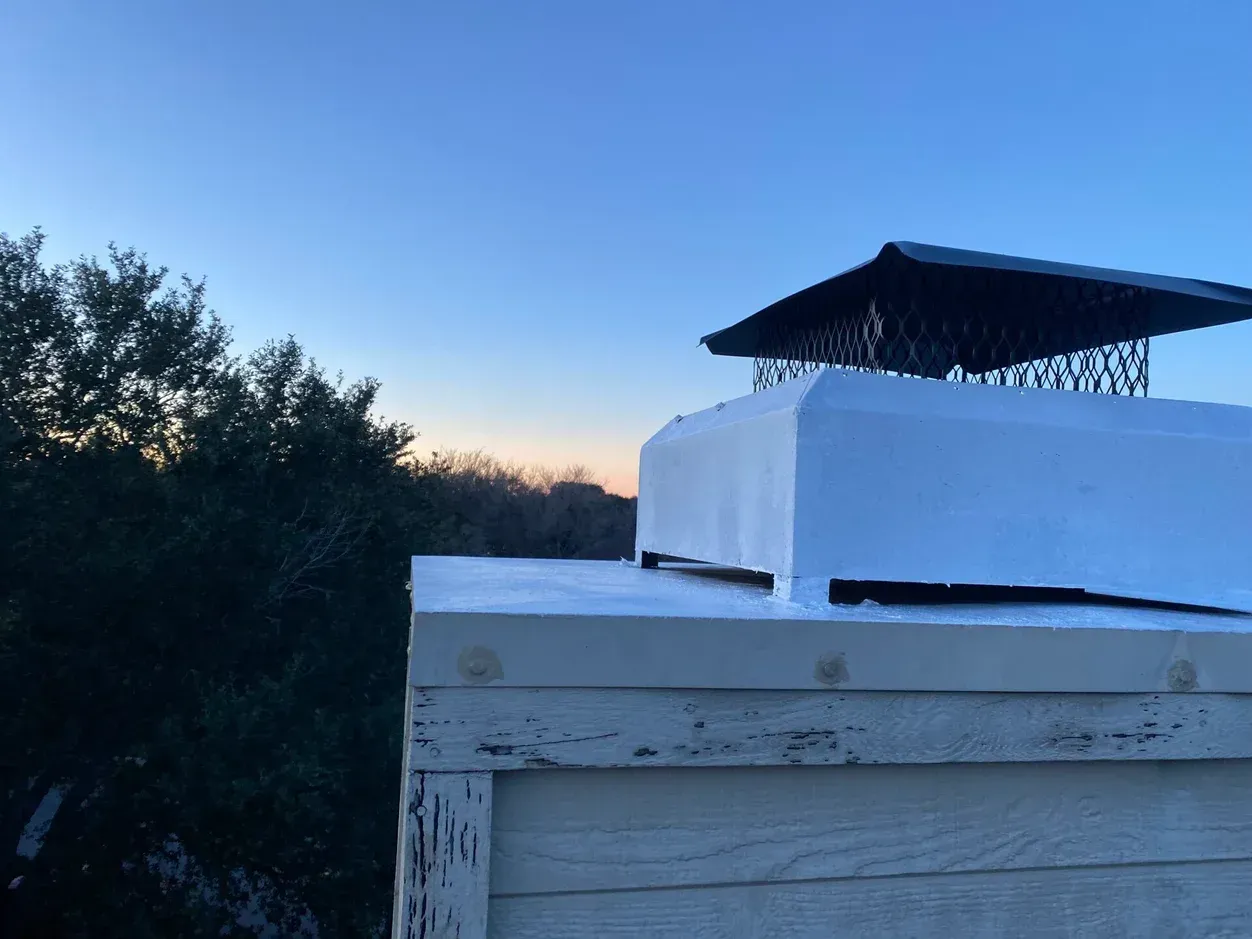 Chimney on a roof with snow and a sunset background.