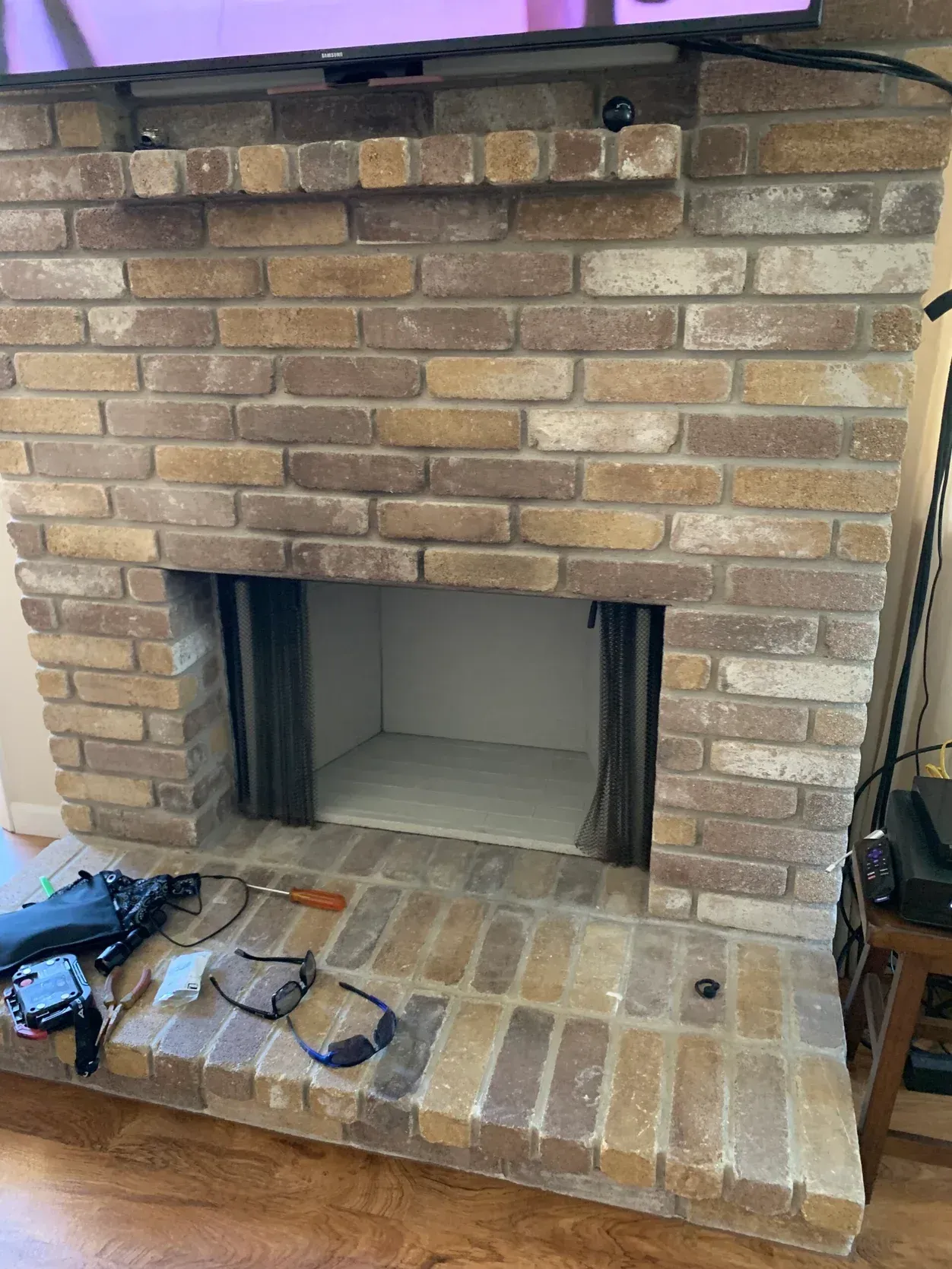 Brick fireplace with empty firebox, tools, and wires on the hearth.