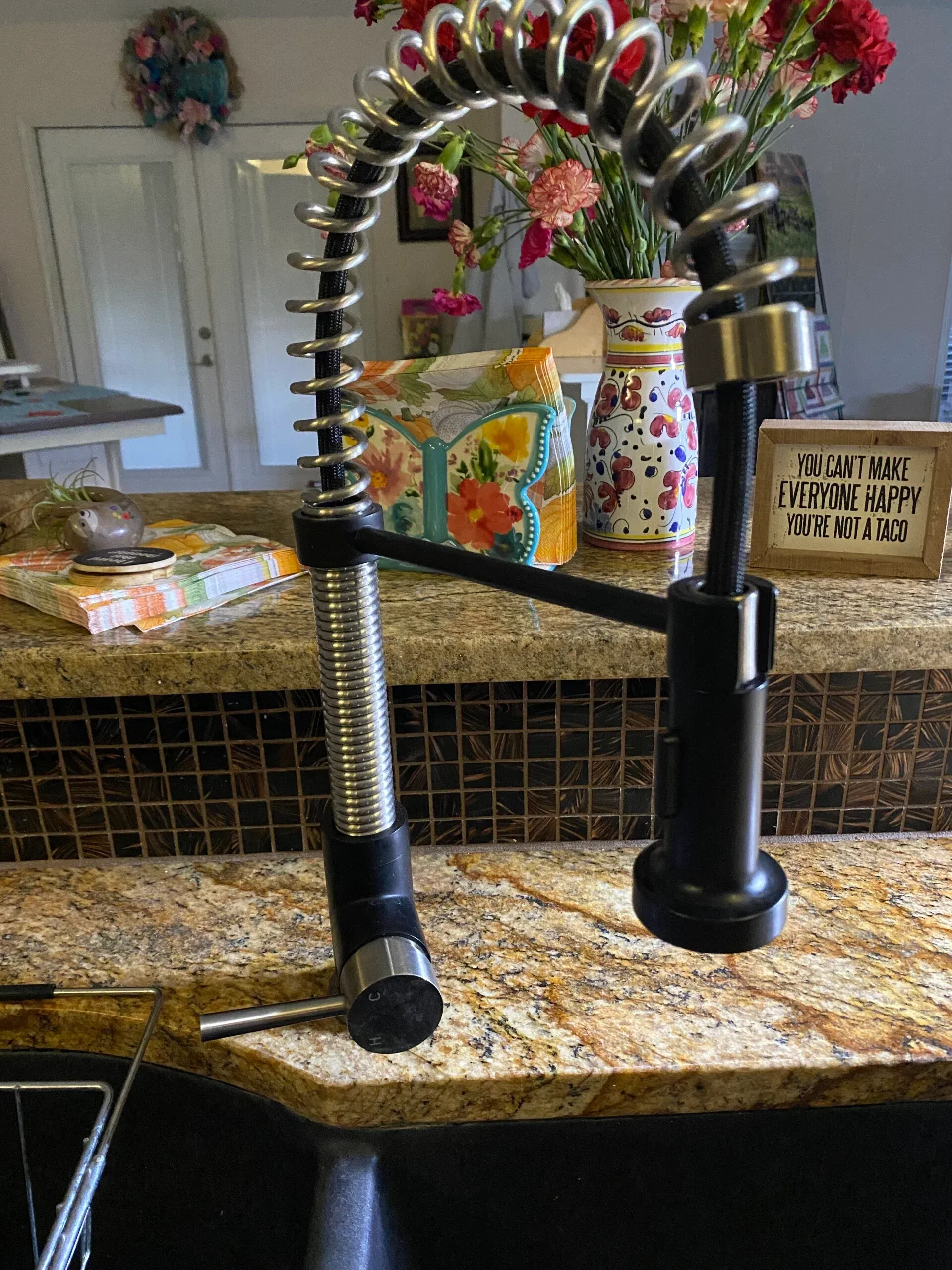 Black and silver kitchen faucet with a pull-down sprayer, set on a granite countertop, flowers in the background.