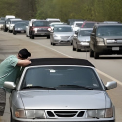 Man leans on silver convertible, stalled on a busy highway with stopped traffic.