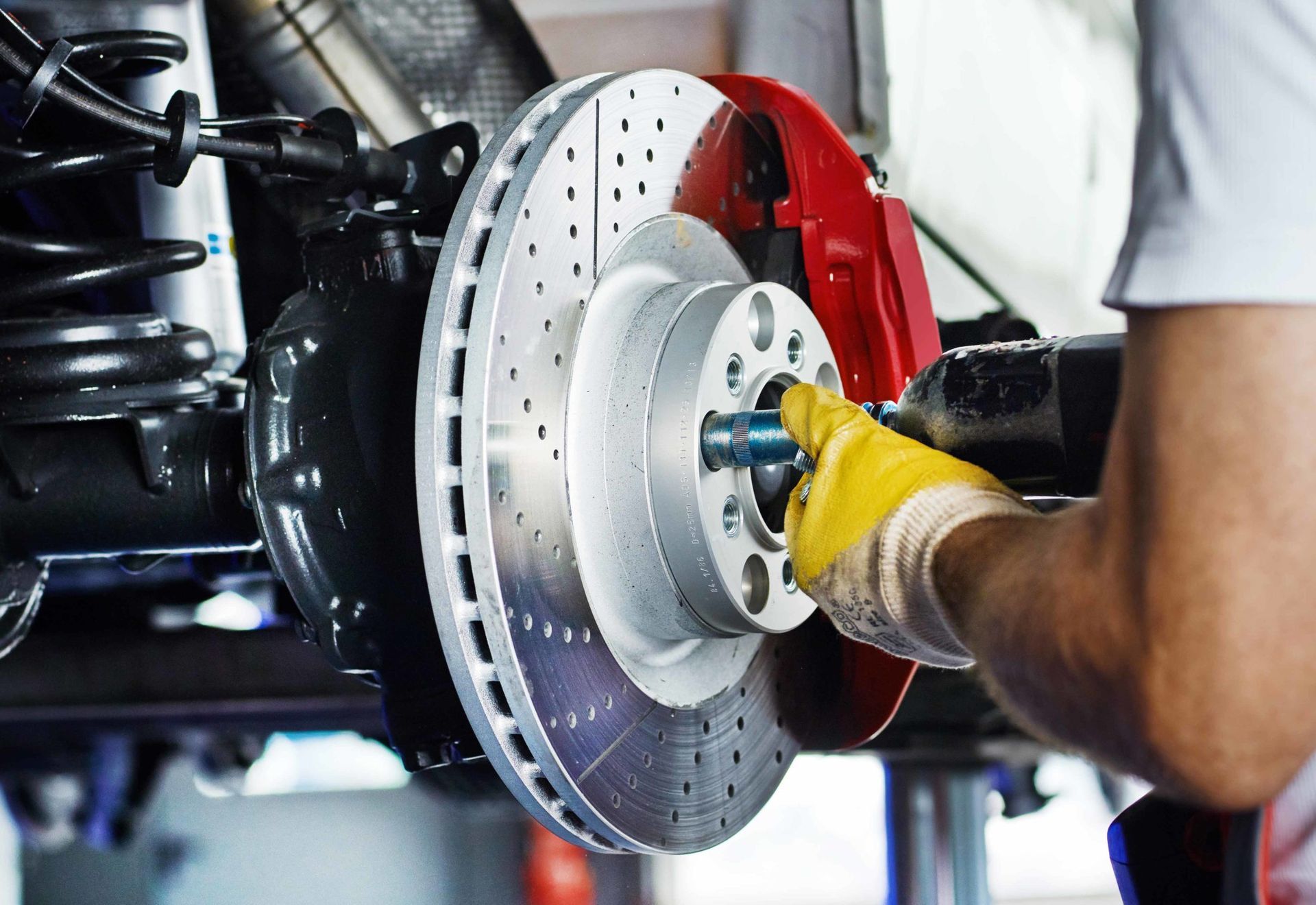 Mechanic working on car brake system, red caliper, yellow gloves, at Huskies Auto Repair Shop