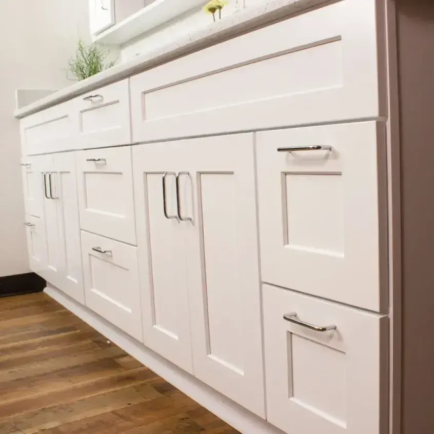 White bathroom vanity with modern silver handles and light countertop over wood flooring.