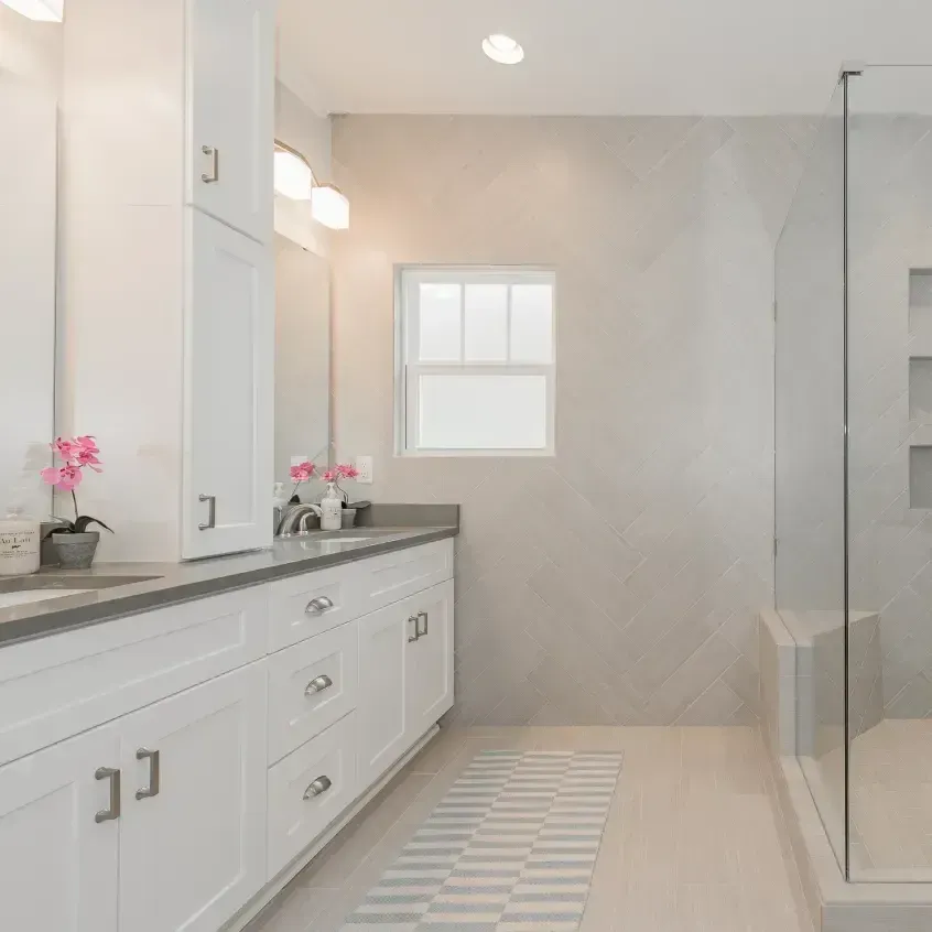 Bright, modern white bathroom with double vanity, glass shower, and gray accents.