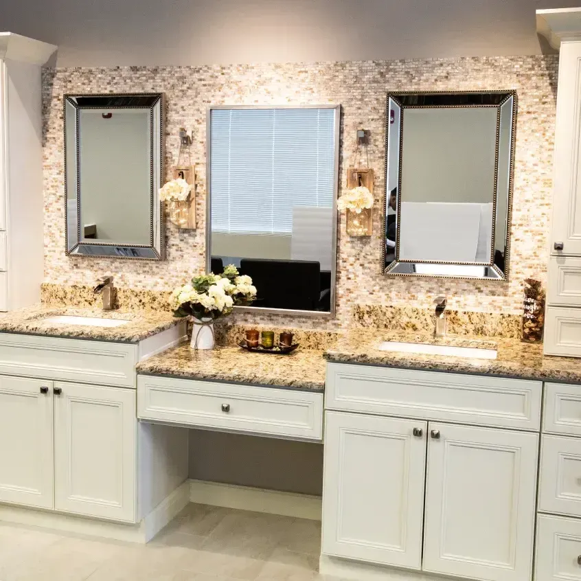 Bathroom vanity with three mirrors, granite countertops, white cabinets, and a mosaic tile backsplash.