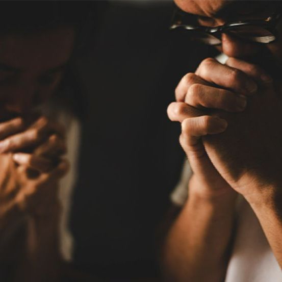 A man wearing glasses is praying with his hands folded