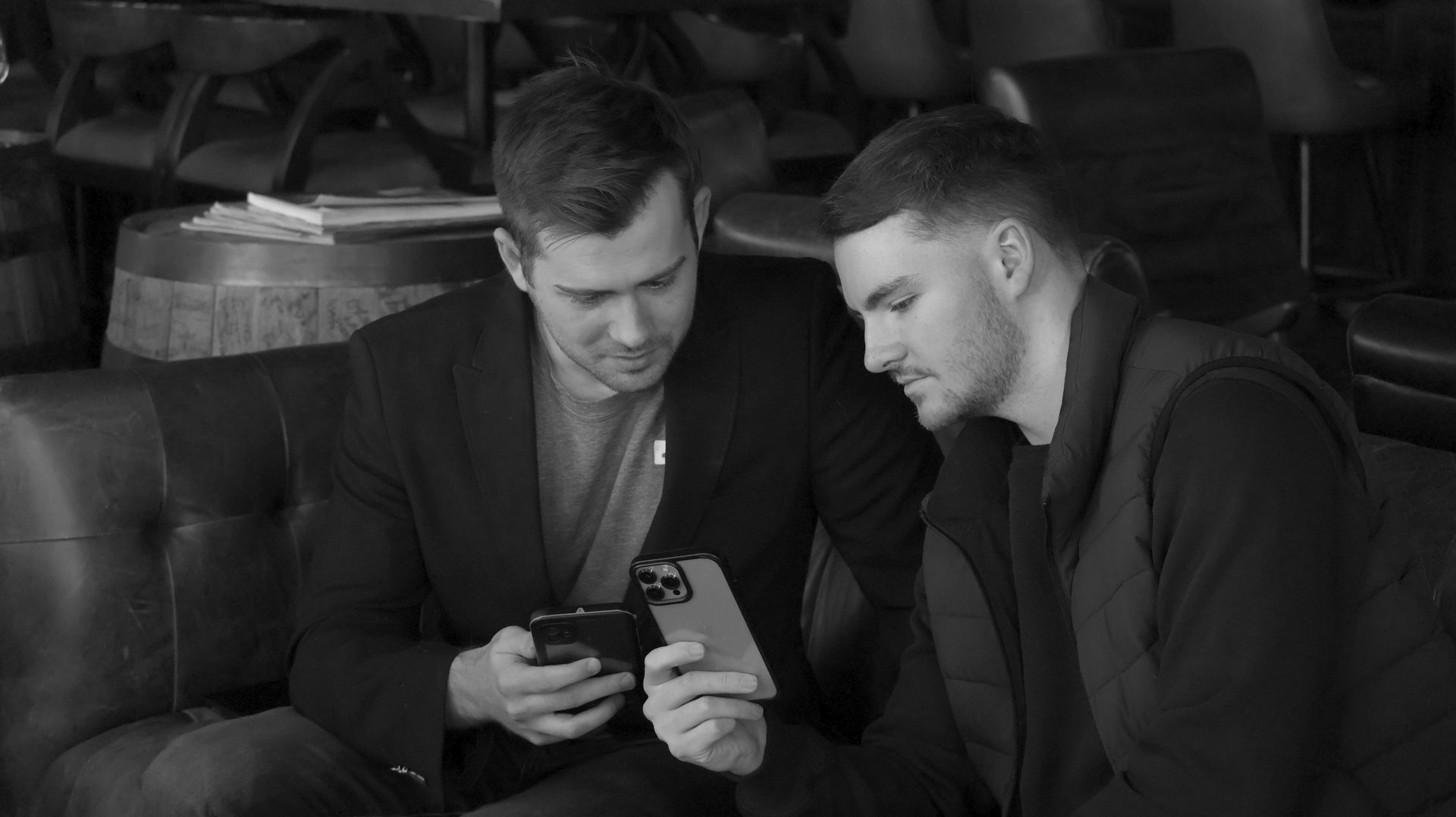 Two men are sitting on a couch looking at their phones.