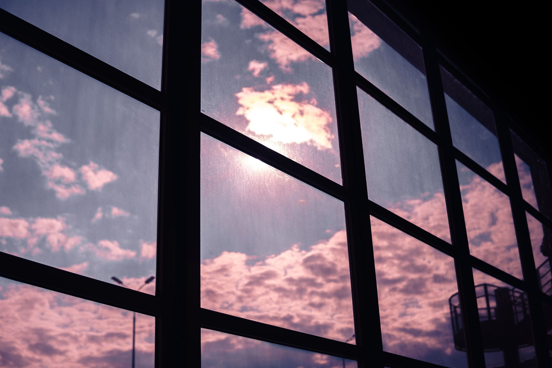 Sky view through a window grid; pink and blue clouds, bright sunlight.