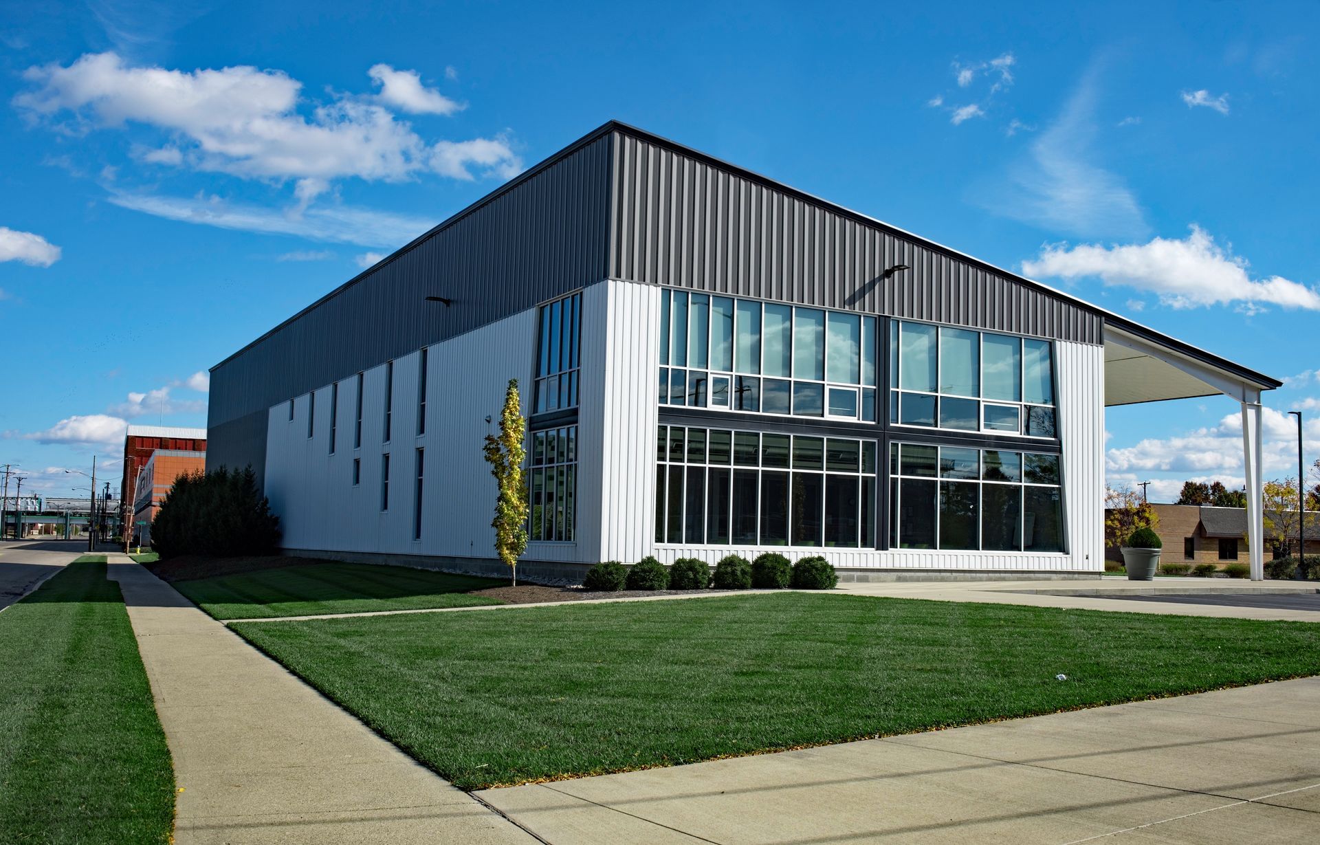 Modern white building with dark gray roof and large windows, green lawn, blue sky.