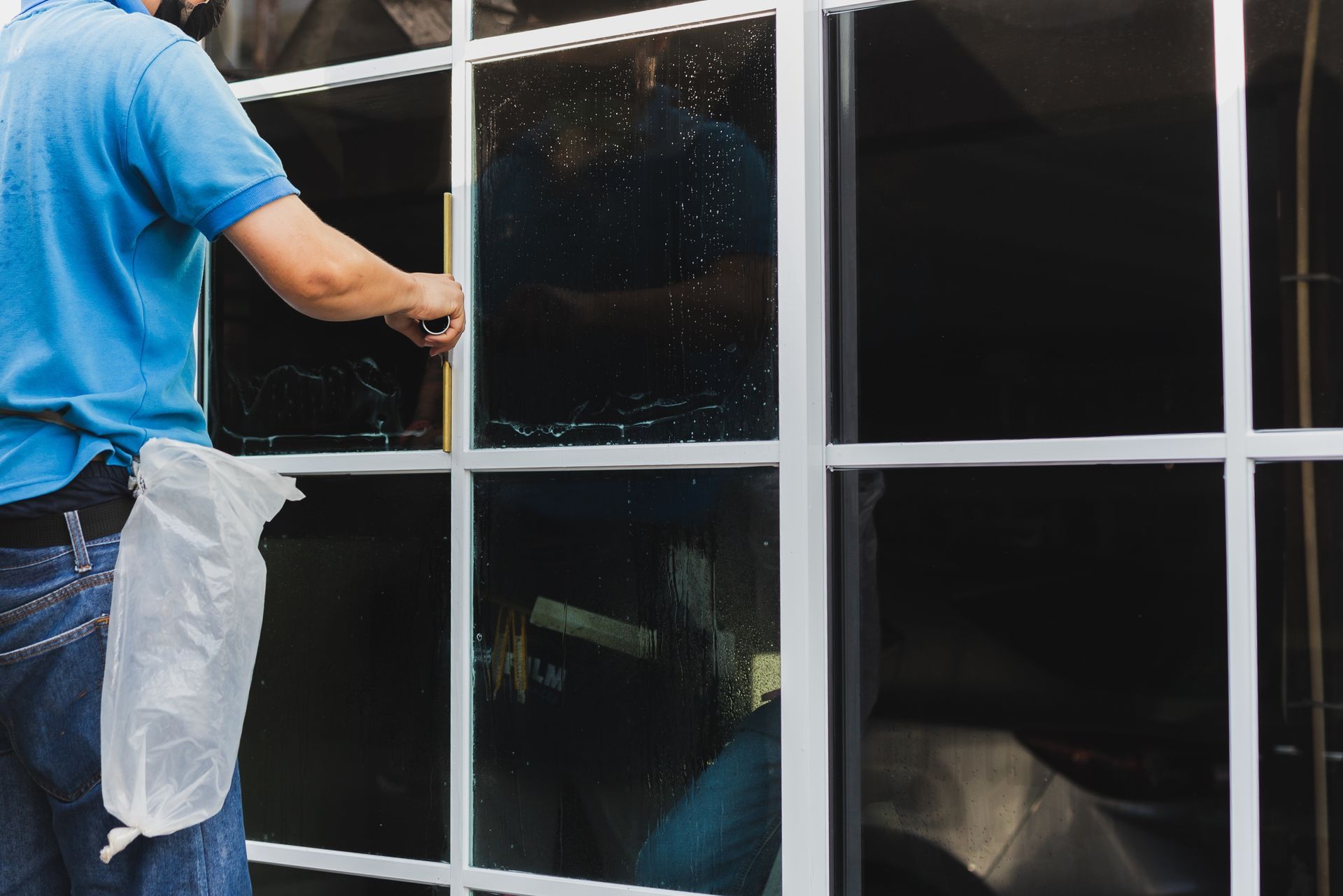 Person applying tint film to a window. The window has white frames, and the person wears blue.