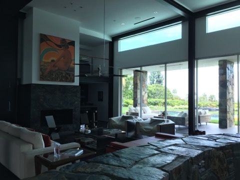 Modern living room with floor-to-ceiling windows, stone accents, fireplace, and artwork; a view to the outdoors.