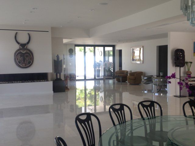 Spacious, modern room with large windows, reflective floor, fireplace, art, and a dining table with black chairs.