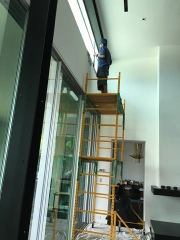 Person on scaffolding working on a window frame, near a glass sliding door.