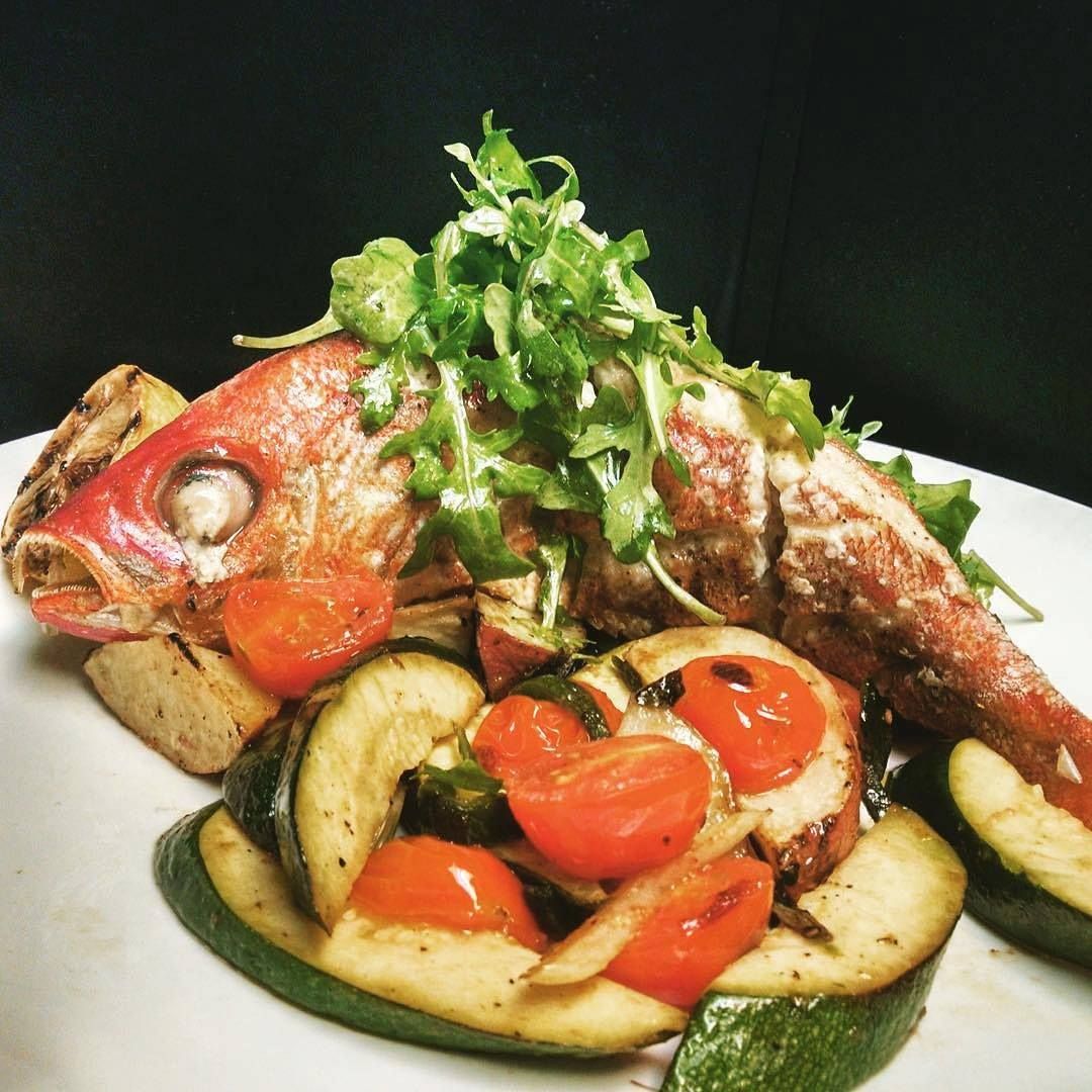 A white plate topped with a red snapper fish and vegetables