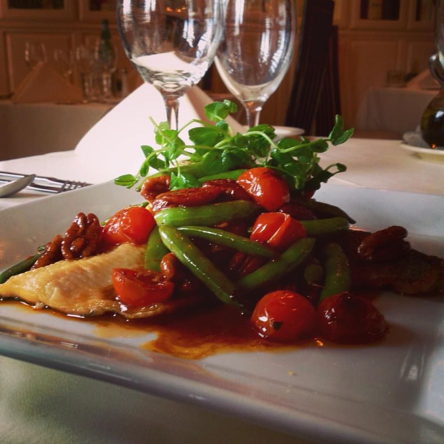 A plate of snapper fish with tomatoes and green beans on a table