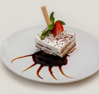 A white plate topped with a piece of Tiramisu and a strawberry