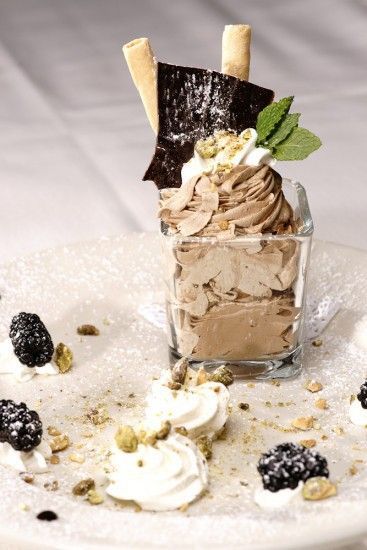 A dessert in a glass on a plate with berries and whipped cream