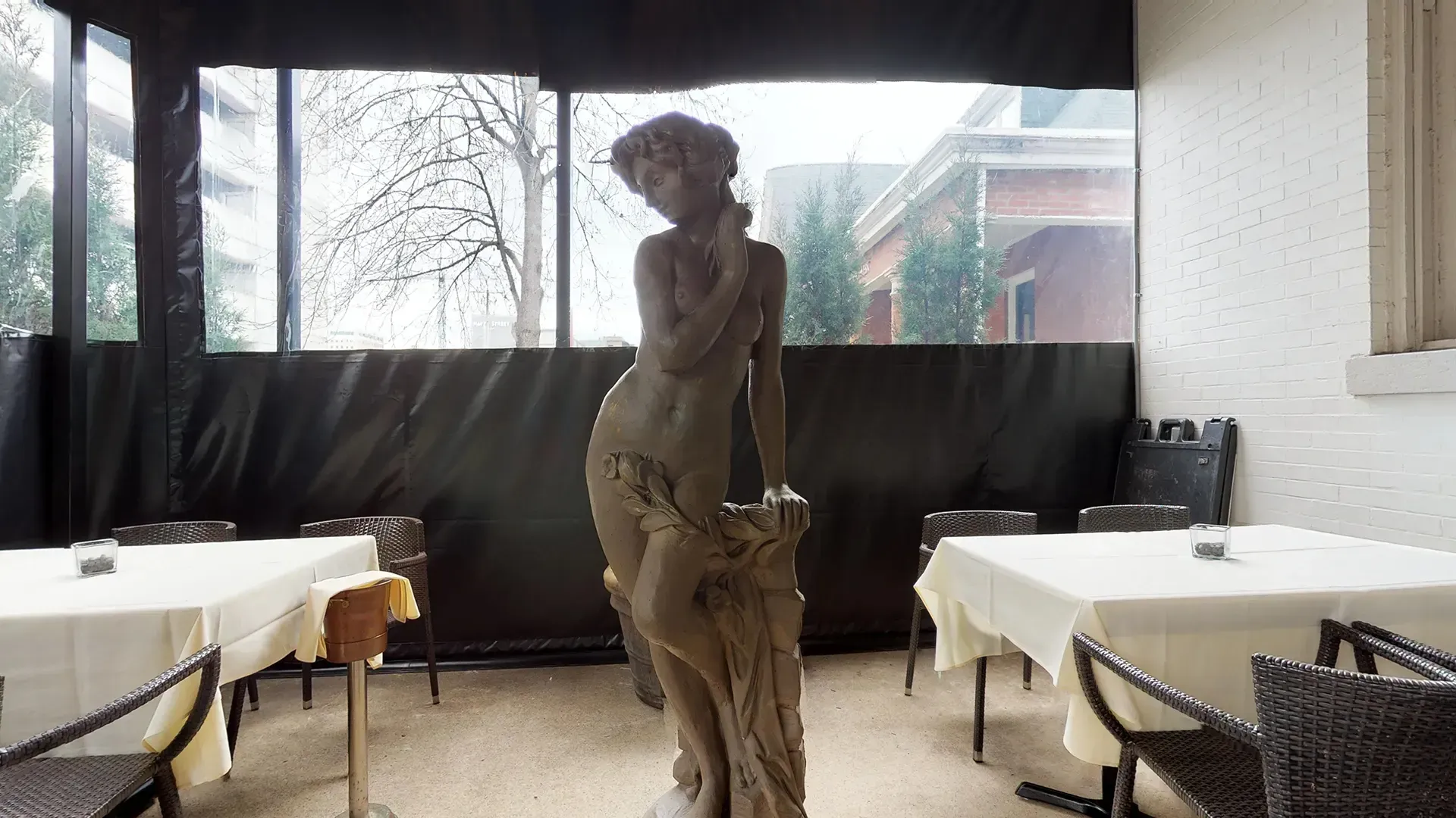 A statue of a woman is standing in a room with tables and chairs.