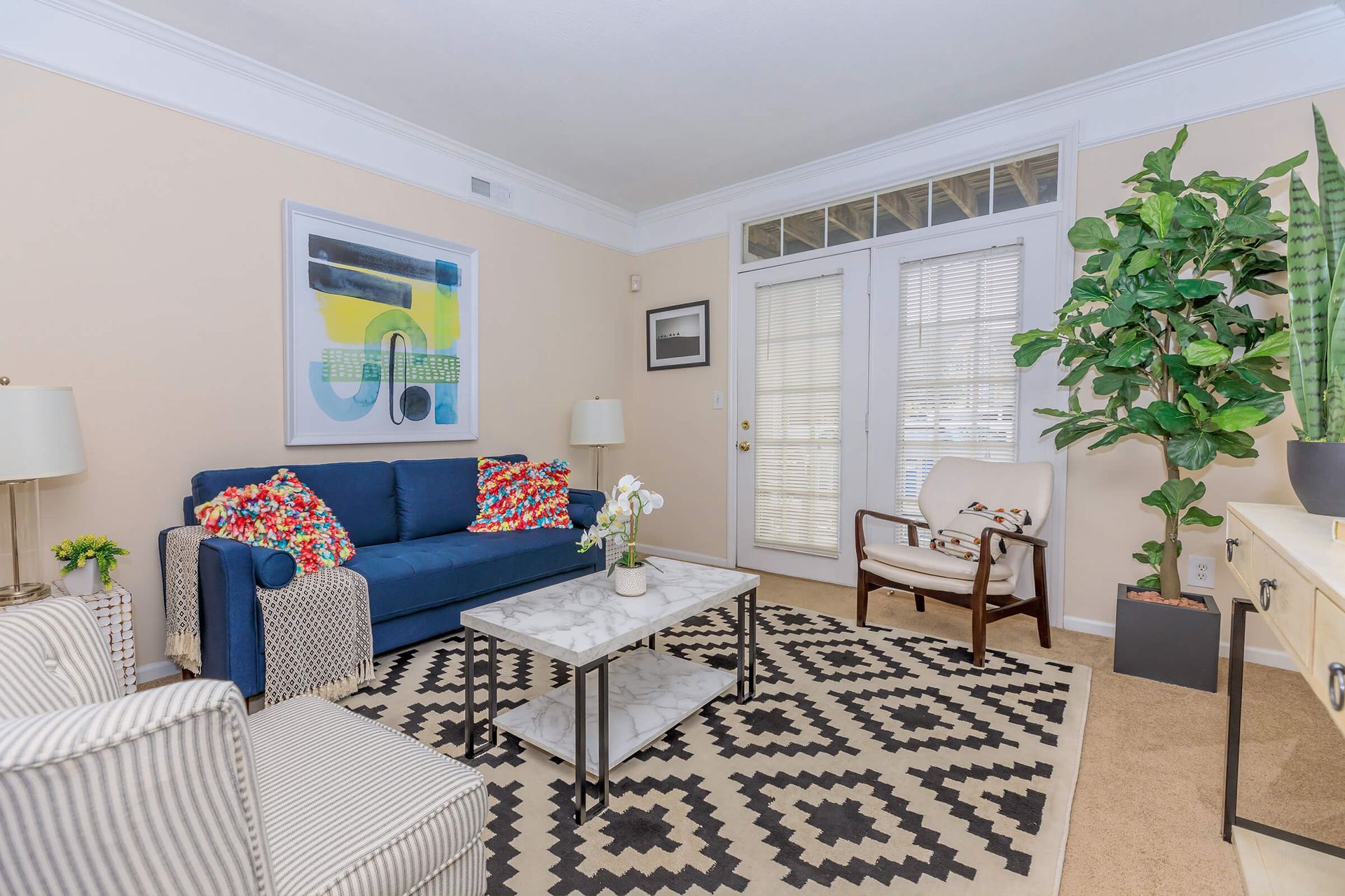 Living room with blue sofa, patterned rug, white armchair, and French doors.