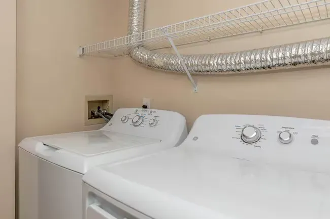 White washer and dryer in laundry room with vent hose, shelf at Quarry in Columbus, OH.