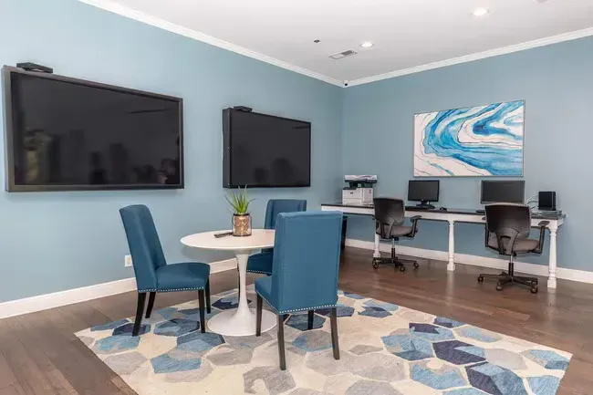 Blue-walled room with table & chairs, two large screens, desktop computers, and abstract art on a patterned rug at Quarry in Columbus, OH.