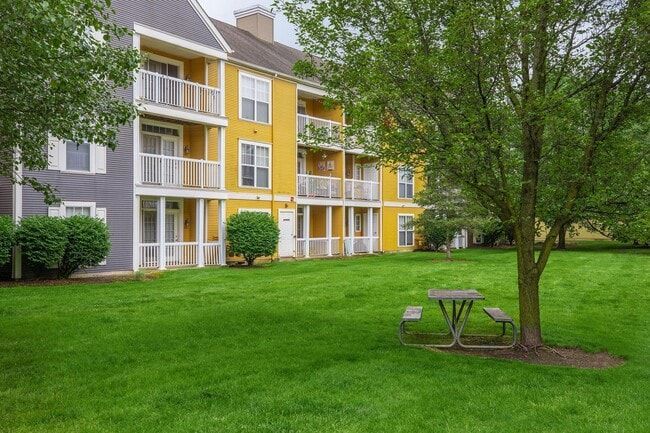 Apartment building with yellow and gray siding; picnic table on a grassy lawn with trees at Quarry in Columbus, OH.