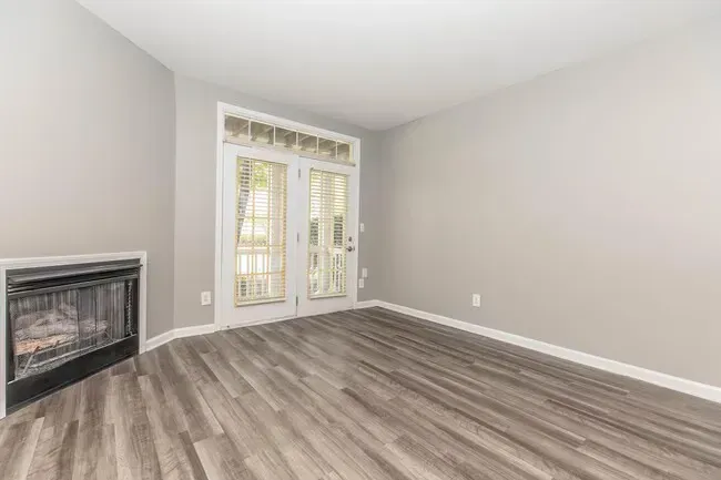Empty gray room with fireplace, wooden floors, and double doors to a balcony at Quarry in Columbus, OH.